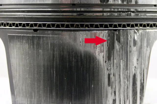 An overheated piston will transfer material from the piston to the cylinder wall, as shown by the arrow.