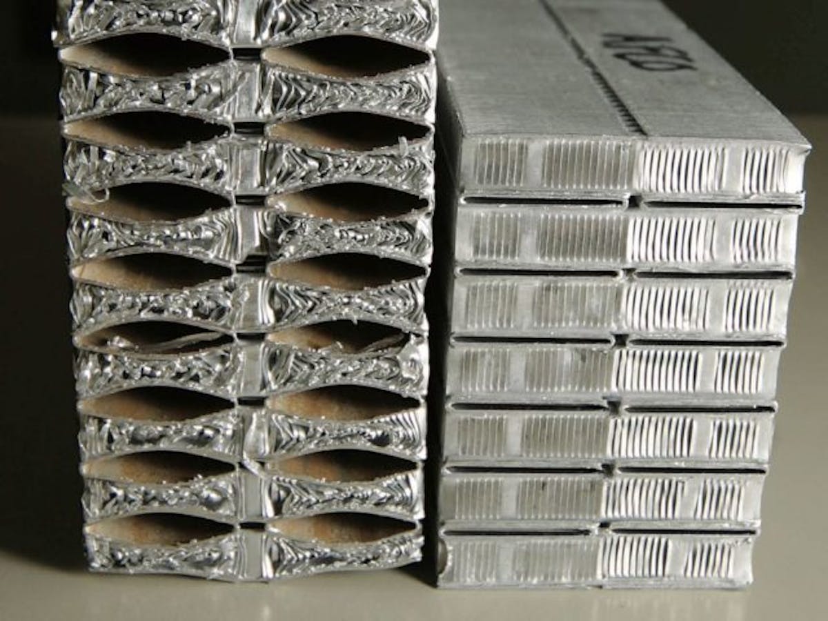This image is the best visual reference for showing exactly what happens when the cooling system encounters pressurization from a head gasket failure. On the right, an undamaged radiator with the thin, flat capillaries as they should be. On the left, the capillary tubes have been blown up and take on a football-like shape, which crushes the fins between the tubes. With these fins collapsed, no air can flow over the capillaries, and no heat can be exchanged. If the radiator can't dissipate heat, it cannot keep the water cool, and problems will arise almost immediately.