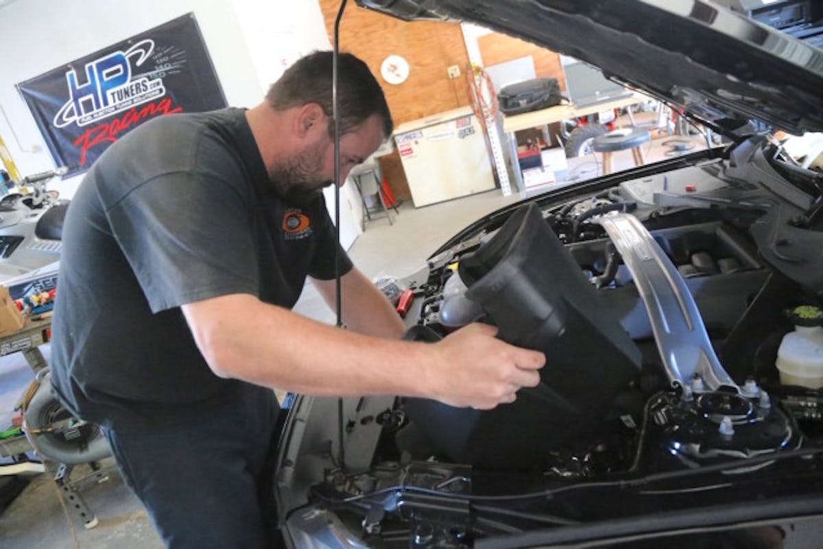 After swapping over the rubber locating spacer, mounting grommet and metal insert from stock box to the JLT, Steven slips the new air box into place and joins it to the factory fresh air scoop in the grille with the include tube. Simply line up the tube and push it over the scoop by pushing down on the rear of the scoop so the tube clears the bump on the scoop.