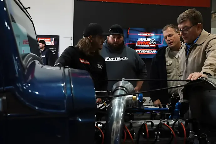 four men looking at an engine of a car