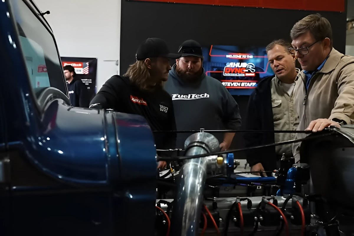 four men looking at an engine of a car