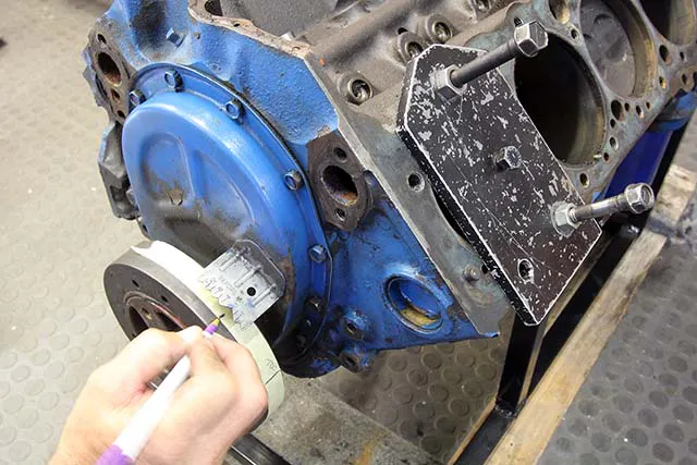 With the cylinder head off the engine, we made up a simple steel plate that bolts to the block and uses a short bolt in the center as a solid piston stop. Bolt the piston stop in place and place a length of masking tape on the balancer and mark TDC. Slowly turn the engine over until it stops. Mark both locations on the balancer.