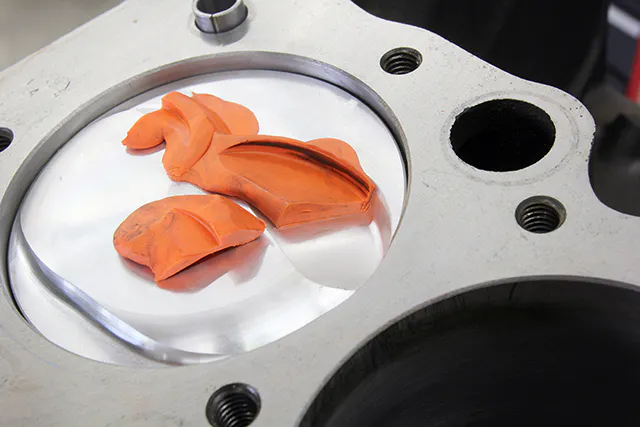 With clay in place over the valve reliefs, rotate the engine several times. Note that the valves have created a depression in the clay that we’ve cut in half with a razor. In this case, the depth clearance was 0.220-inch for the intake but only about 0.090-inch for the exhaust. Also note that the radial clearance for the intake appears to be tight – it is difficult to measure but appeared to be about 0.080-inch. This may require more accurate measurement.