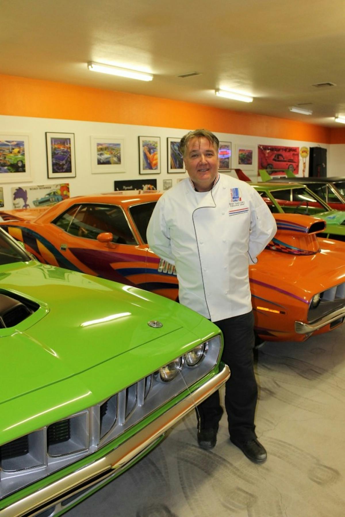 Dressed in his kitchen attire, a very proud Chef Brad Toles poses in front of his favorite vehicles, plain and fancy ’71 Hemi ’Cudas, along with other legendary Mopar missiles.