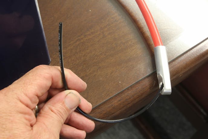 The black discharge hose is plumbed through the negative terminal in the lid and wound through the cable where it is shown here exit-ing the cable end. All that’s left is to drill intersecting holes in the mounting bolt and then allow the bolt to exit into the intake manifold.